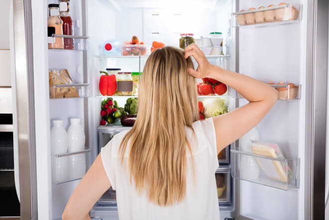 Frau steht fragend vor ihrem übel riechenden Kühlschrank